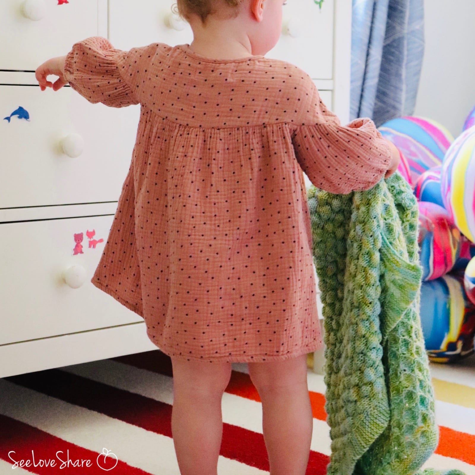Lifestyle photo of the bubble stitch knit baby blanket draped over a baby