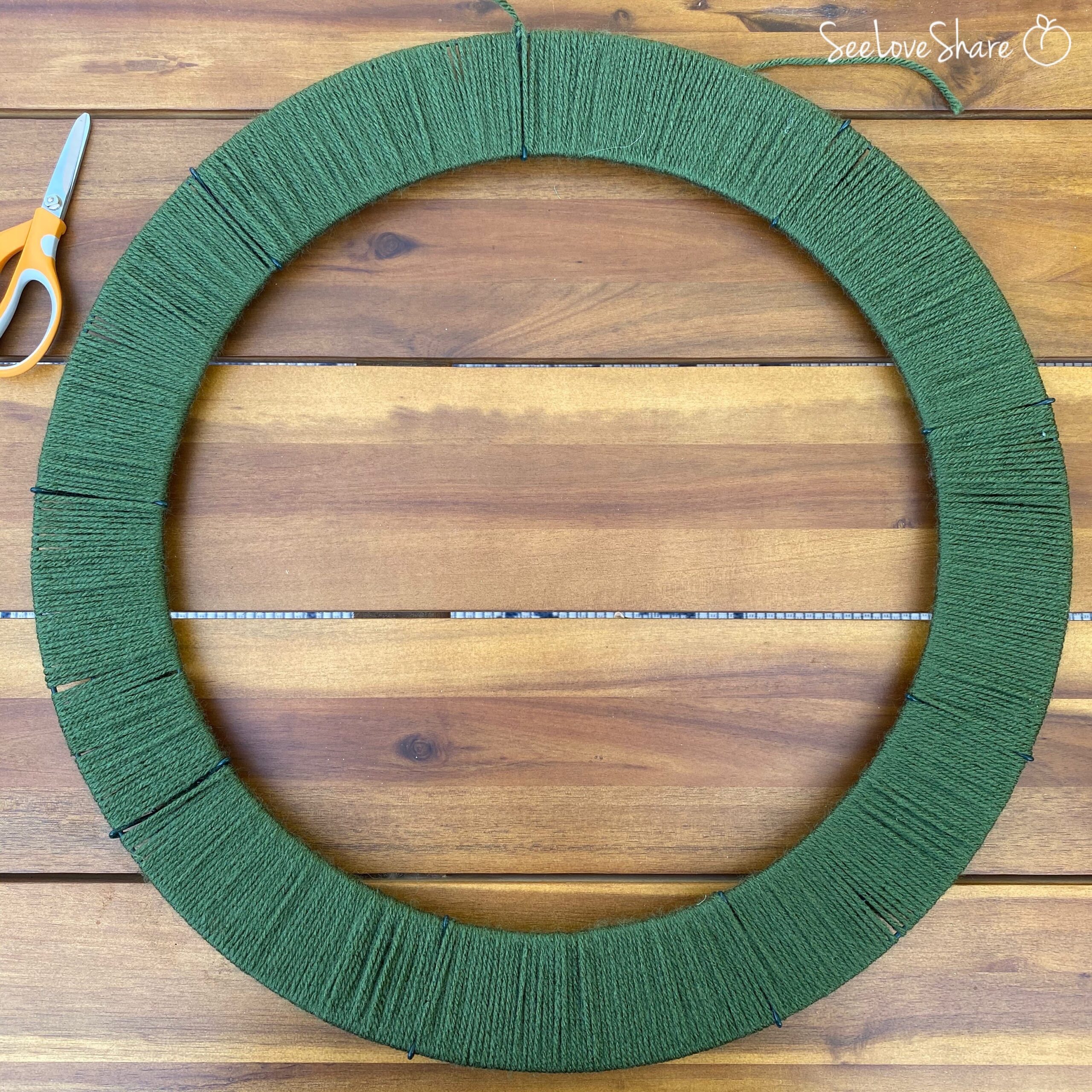 Wire wreath frame fully wrapped in green yarn ready for the crochet pumpkin embellishments
